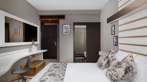 A contemporary bedroom at The Atara, Gurugram featuring a comfortable bed, a functional desk setup, and a wall-mounted television