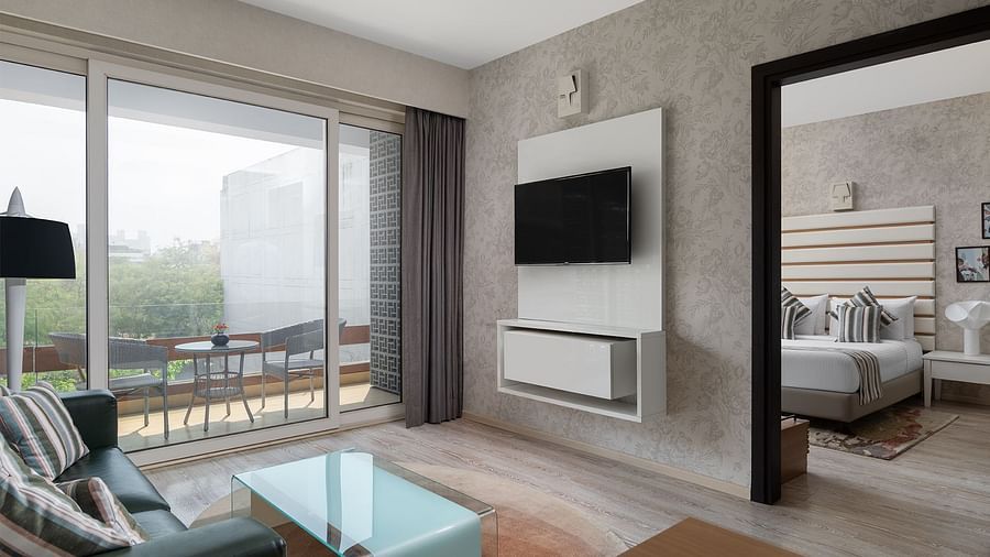 A modern living space at The Atara, Gurugram presented with a wall-mounted TV, a light blue couch with a glass coffee table, and a large sliding glass door that opens to a balcony