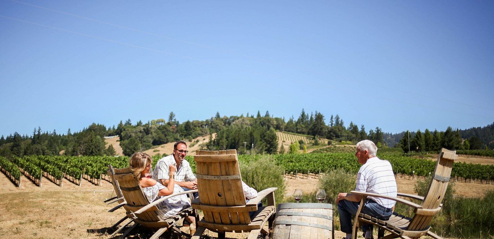 wine glasses filled with red wine on a table outdoorswith people sitting on a few chairs