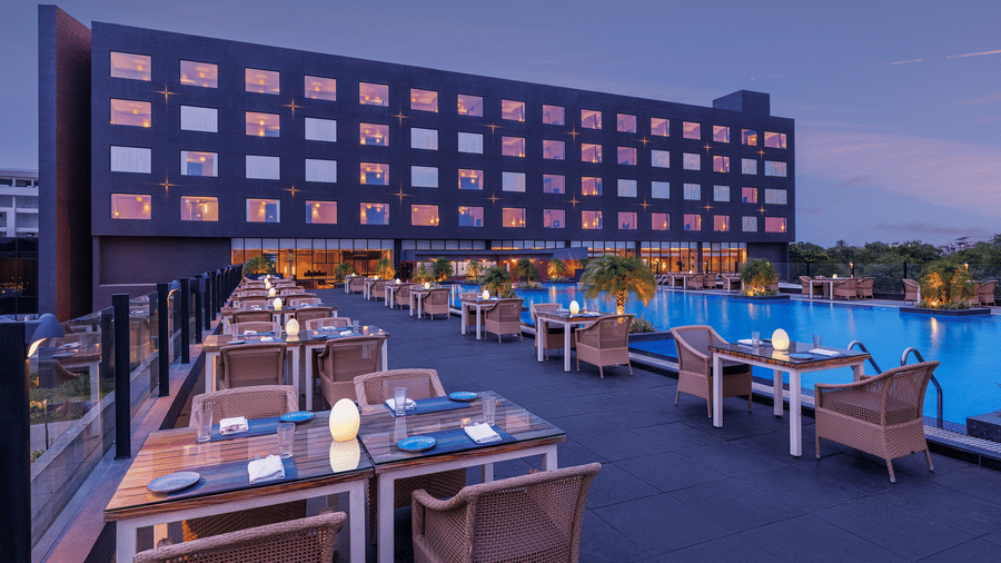 Poolside seating arrangement at Splash Bar & Grill, the best place for lunch in Indore,with the building of Essentia Luxury Hotel, Indore, in the backdrop in the evening