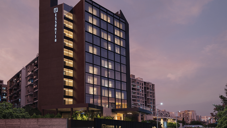 Facade of Essentia Premiere, Pune with lights on during twilight.