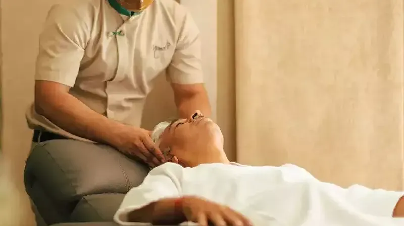 Male spa therapist giving a facial massage to a client lying on a treatment chair, in a softly lit room at Karma Chalets.