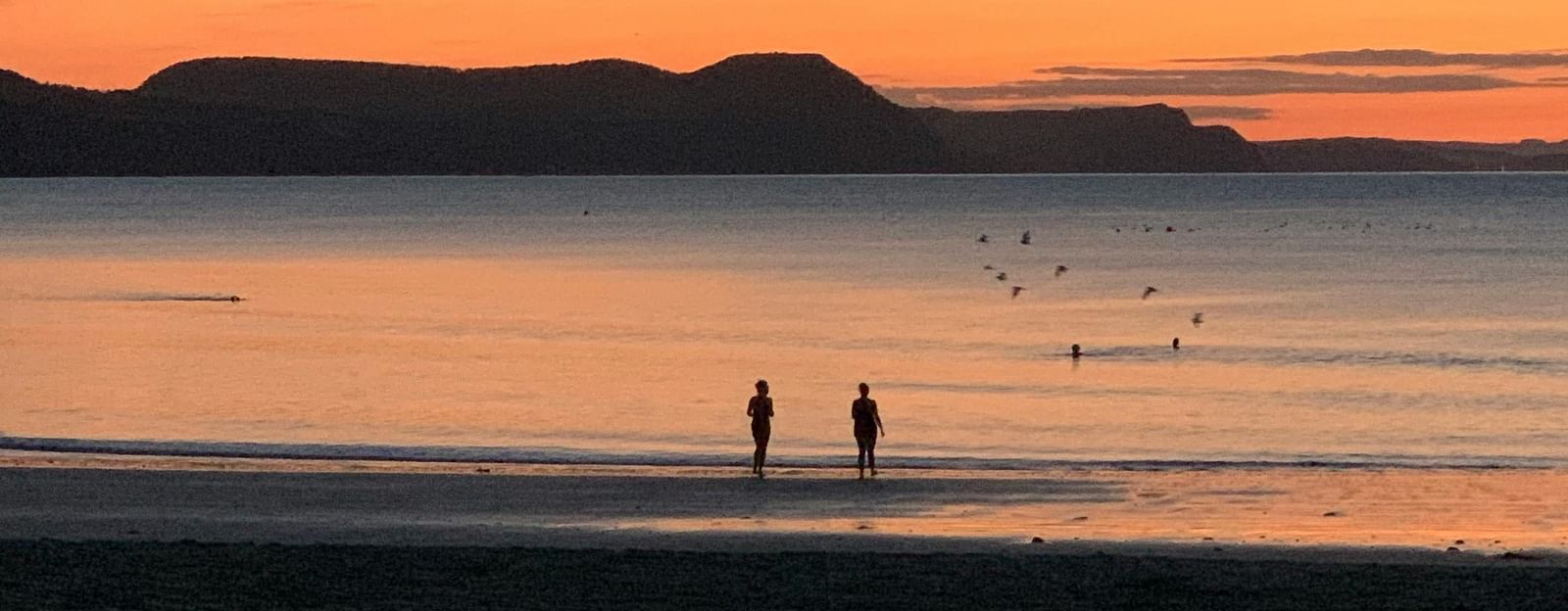 two people walking on the beach during sunset