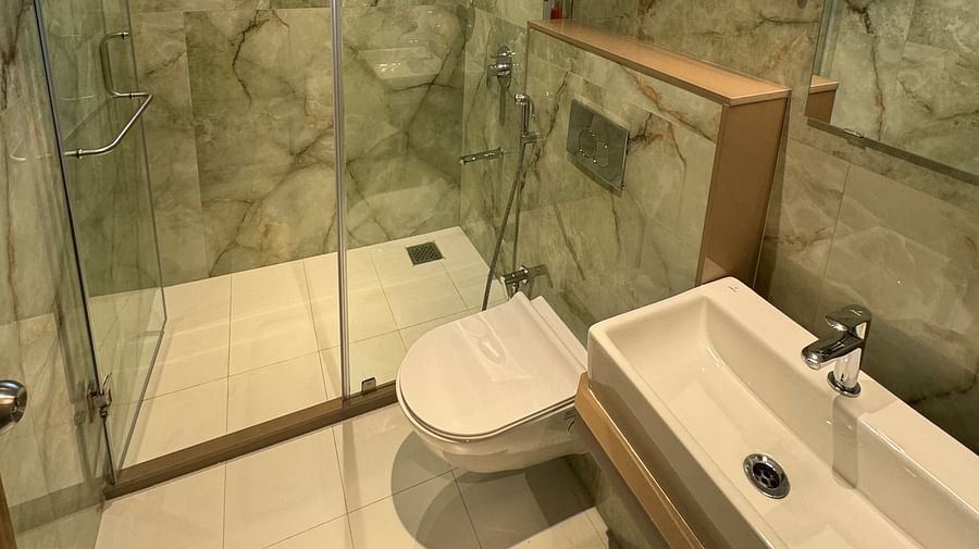 A bathroom with green marble, glass shower, toilet, and sink with a window.