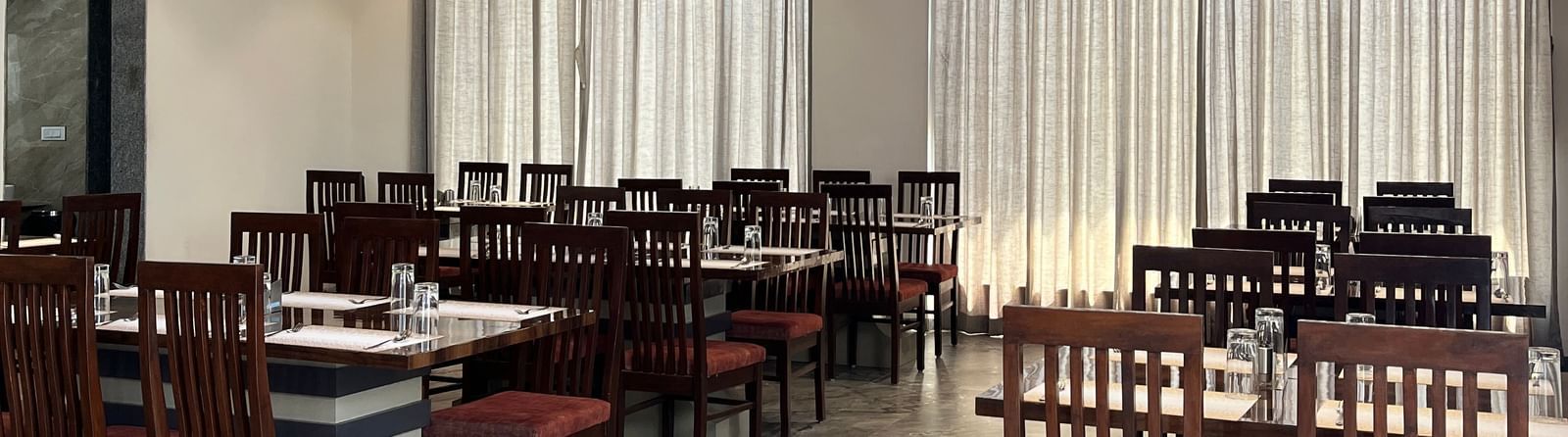 Close up of a row of dining tables neatly arranged in front of long closed curtains at Daksh The Valley Resort, Saputara