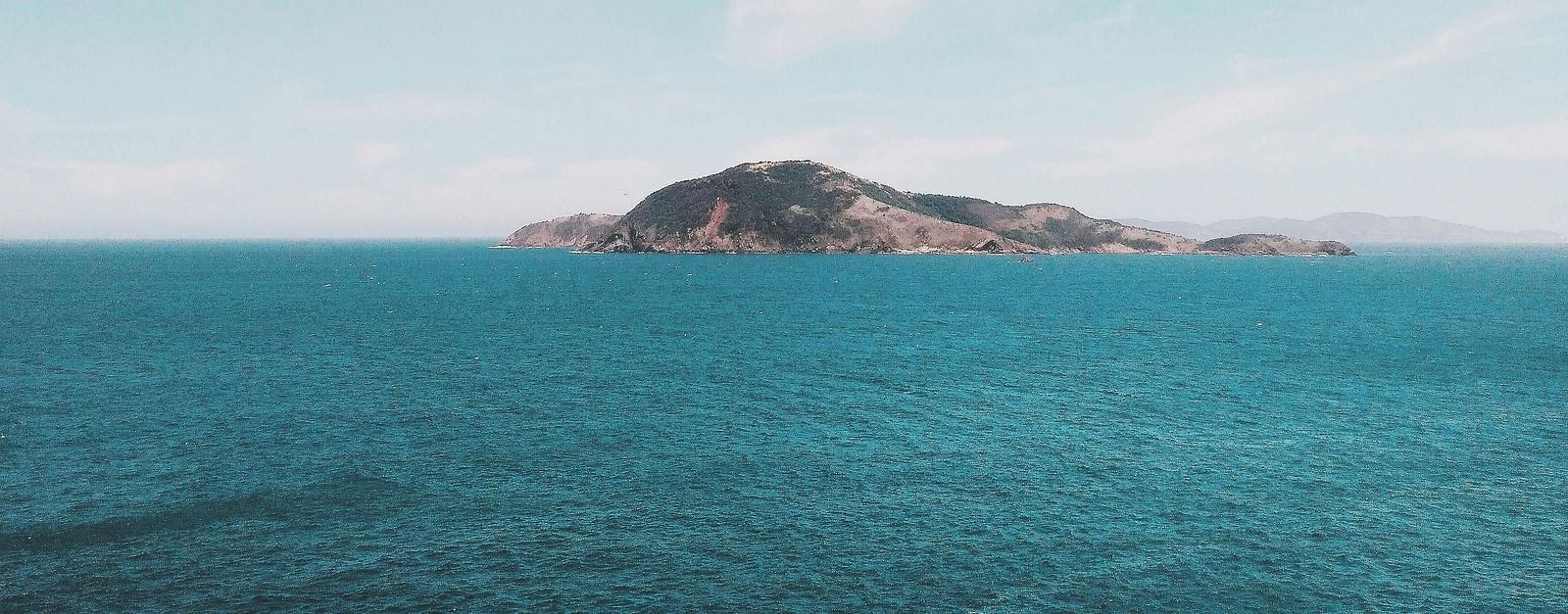 Clear turquoise sea with a distant island and a flock of birds flying overhead.