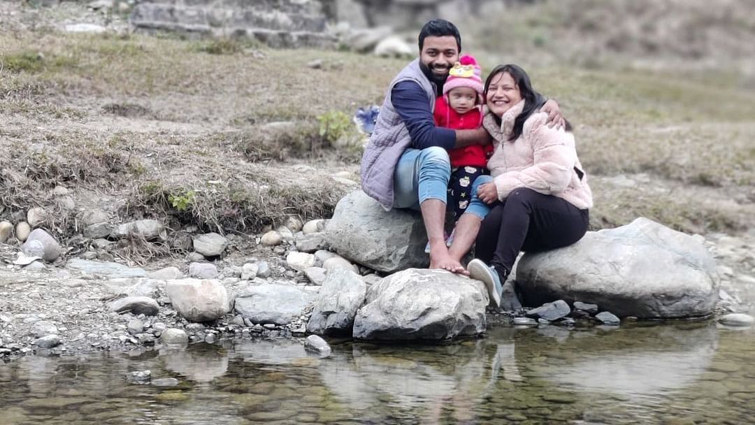 A couple holding a child and sitting on a rock by the brook at The Sylvan Retreat, Dehradun.
