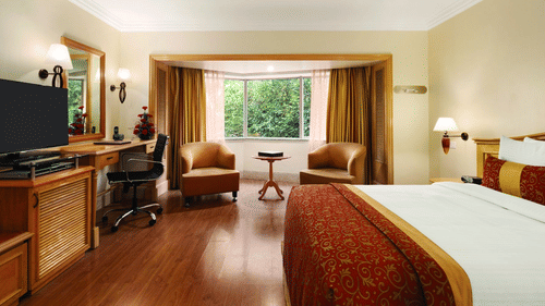 An image of a Deluxe Room featuring bed, flat screen TV, lamps, work desk, chair, sofa set and table - Ramada Plaza by Wyndham Palm Grove