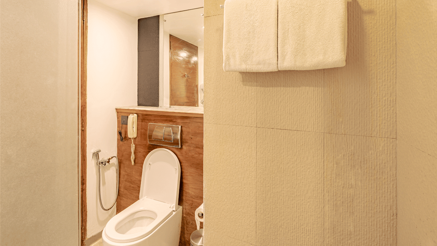 View of a bathroom at The Promenade Pondicherry with a WC, overhead towel shelf, neatly folded towels, and soft warm ambient lighting.