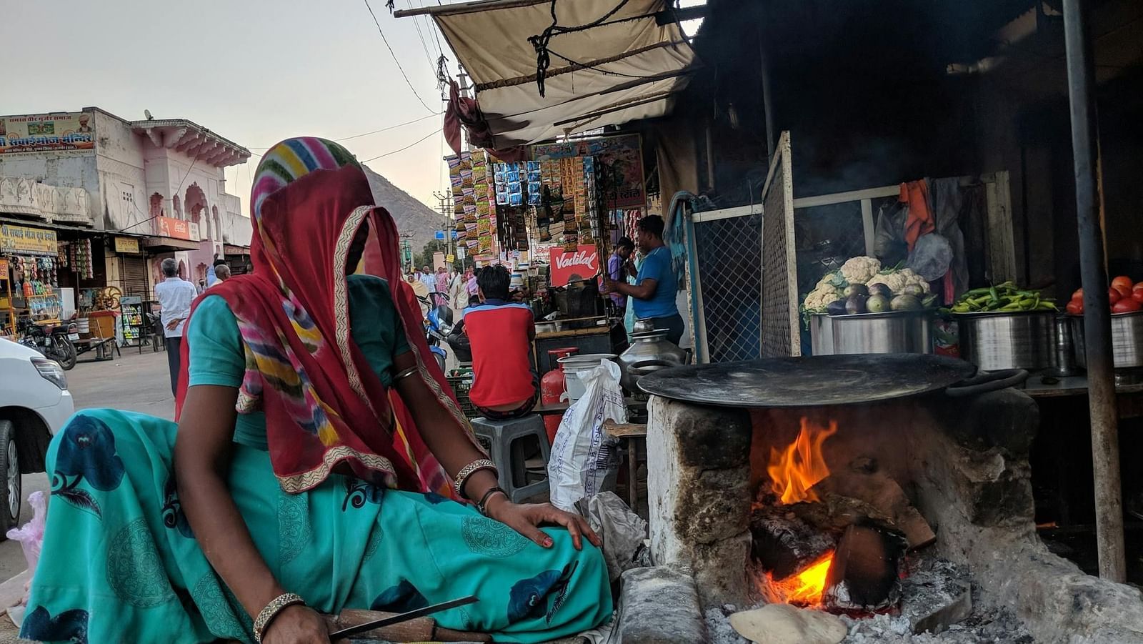 An image of a woman sitting by a fireplace with vegetables on the side kept ready for cooking