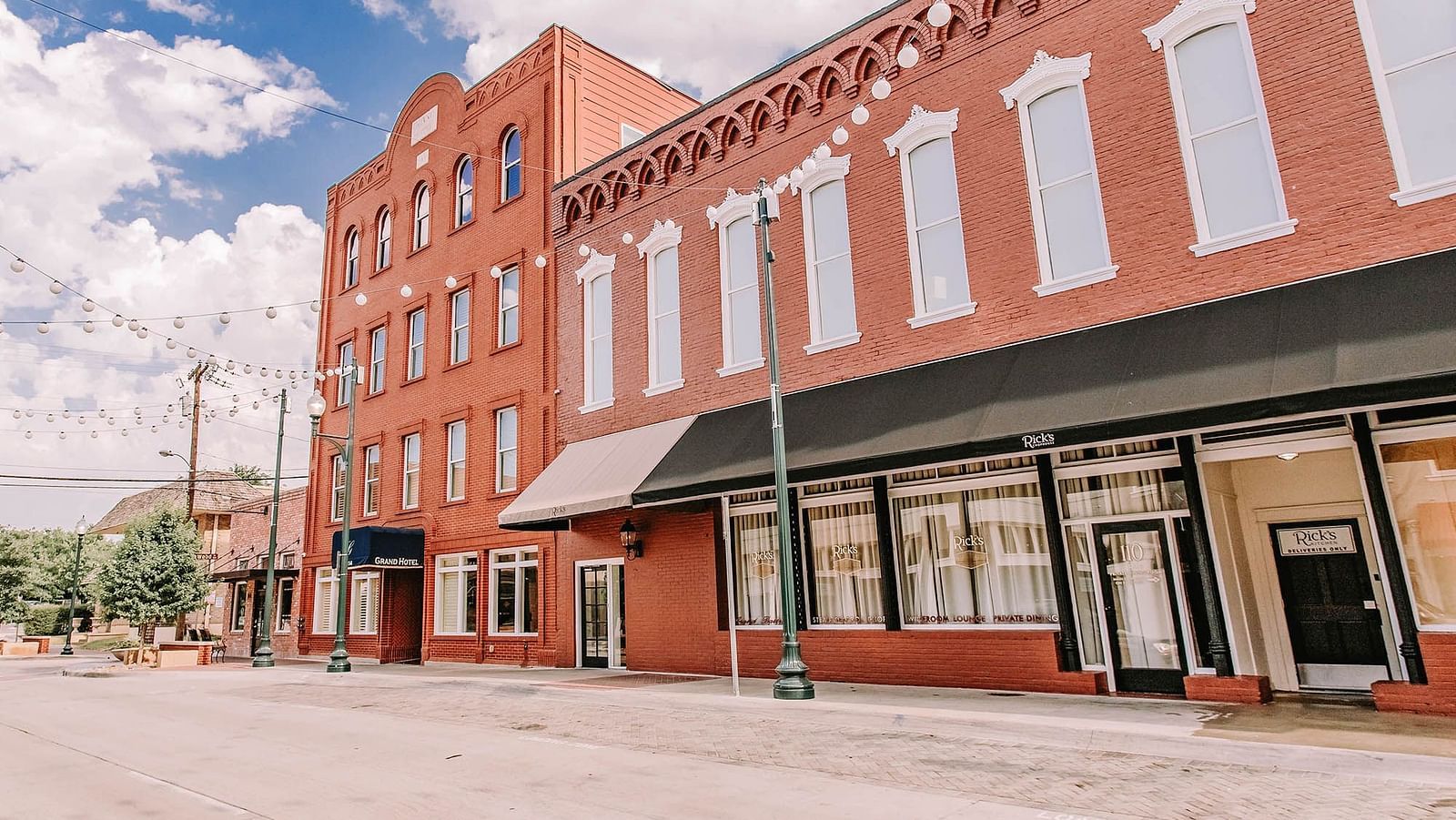 A brick building with large windows, a awning, and a quiet street.- The Grand Hotel & Ballroom, McKinney