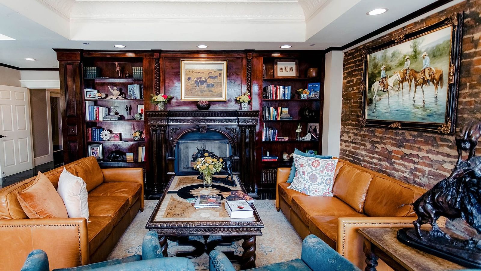 A warmly lit lounge with couches, chairs, a fireplace, and paintings decorating the space.- The Grand Hotel & Ballroom, McKinney