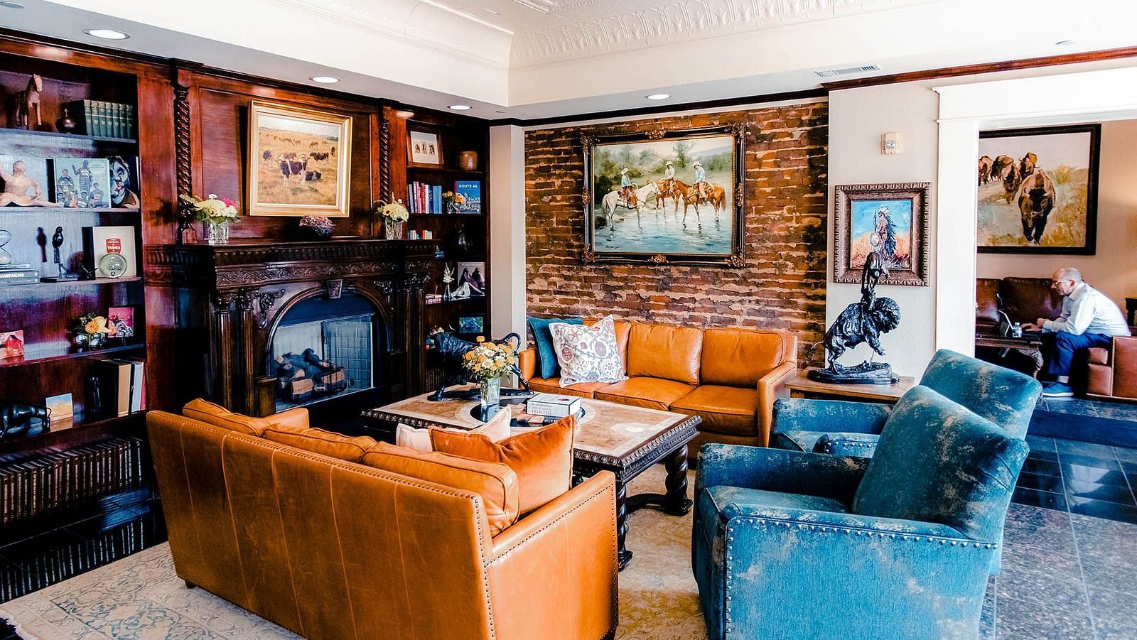 A  lounge with bookshelves, neat seating, and framed paintings on the walls.- The Grand Hotel & Ballroom, McKinney