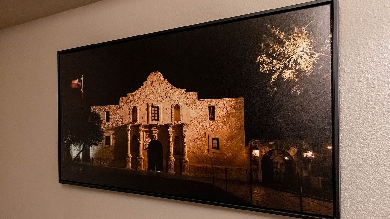 A framed photograph of a historic stone building with fireworks illuminating the sky, adding a dramatic visual effect.- The Grand Hotel & Ballroom, McKinney