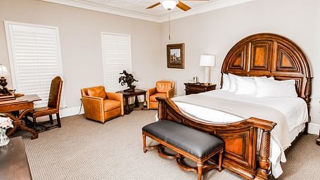 A traditional bedroom featuring a wooden bed, elegant decor, and a ceiling fan, providing a comfortable and timeless space - The Grand Hotel & Ballroom, McKinney