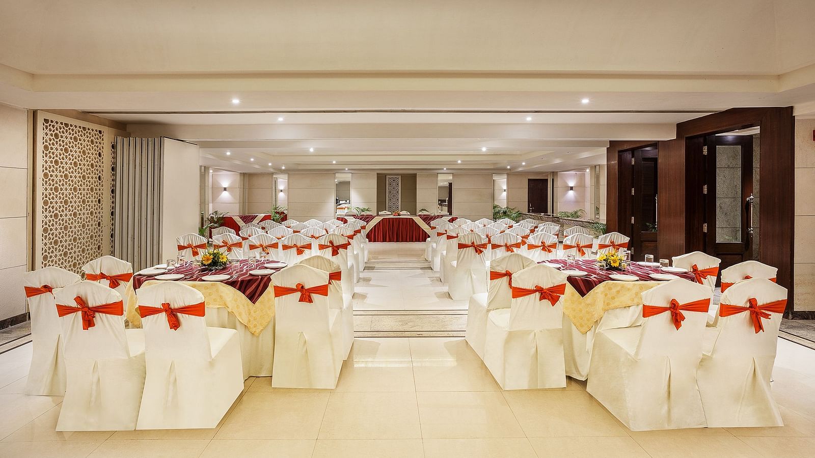 an image of an event space showing a well-spaced seating arrangement with white chairs tied with red bows - The Manor, Bareilly