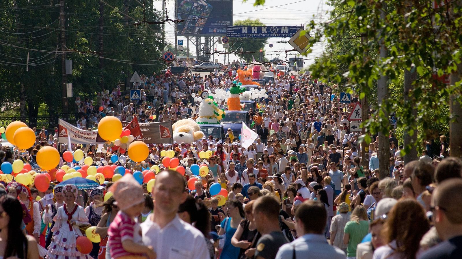 An overview of a parade on a street that is filled with people, floats and balloons.