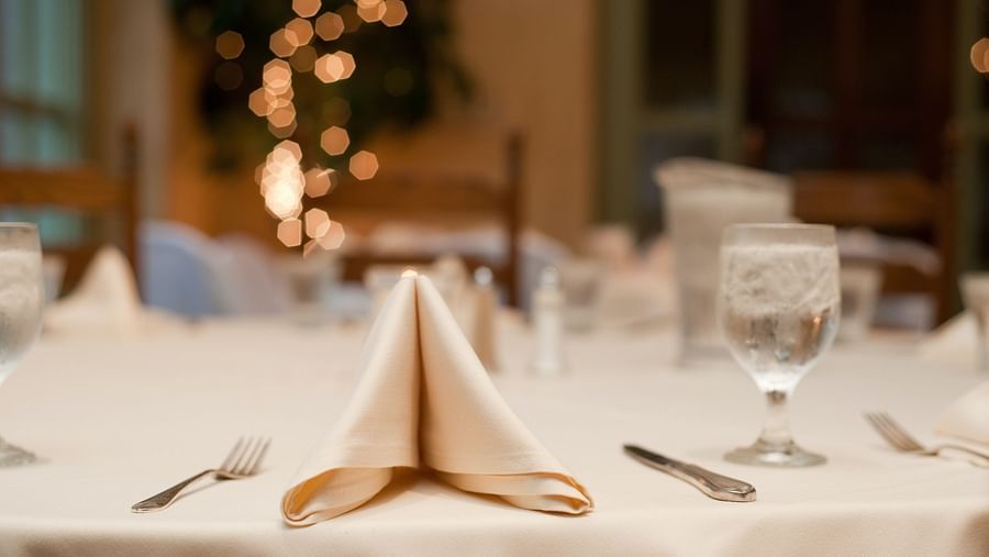 a napkin beside utensils and a glass on a table in a banquet hall set up for an event