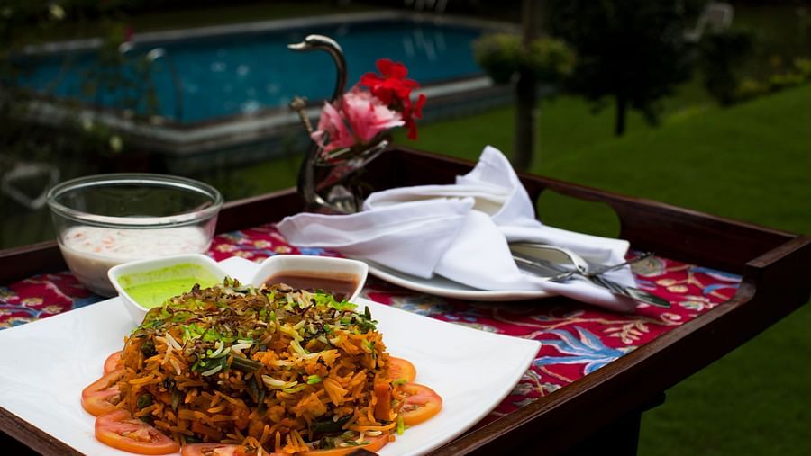 A plate of biryani with accompaniments, served outdoors with a pool in the background.