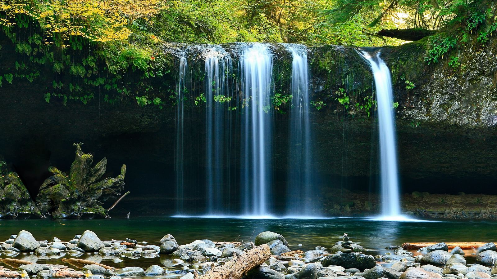 A waterfall cascading down to a waterbody with rock and nature surrounding it