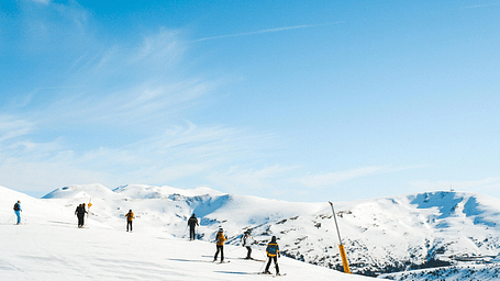 people scattered around warmly dressed with their skiing gears on a snowy plain with mountains in the background