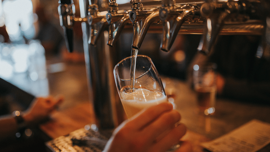 Close up of a hand holding a glass being filled with draft beer at a bar.