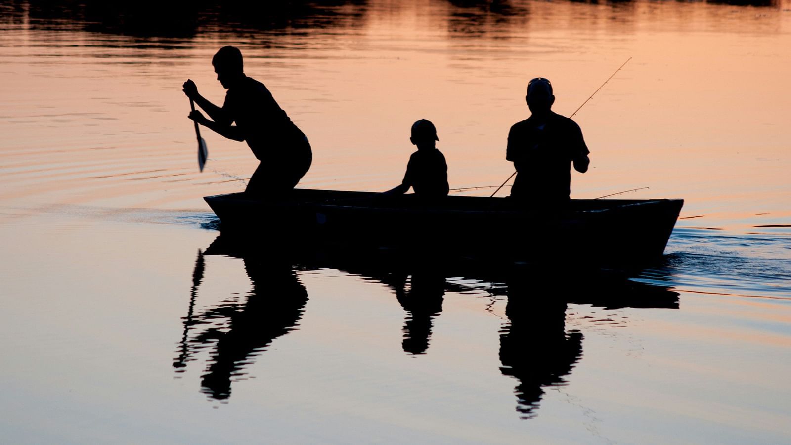 Three people sitting in a boat on a waterbody trying to fish.
