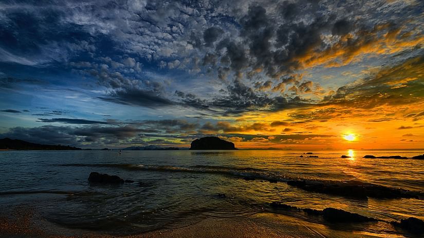 Sun setting in the distance and the sky showing hues of blue and orange with waves crashing into the sand
