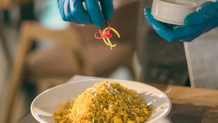 A plate full of corn rice being served by the waiter garnishing  it at The Bridge - Clarks Inn Suites Jaipur