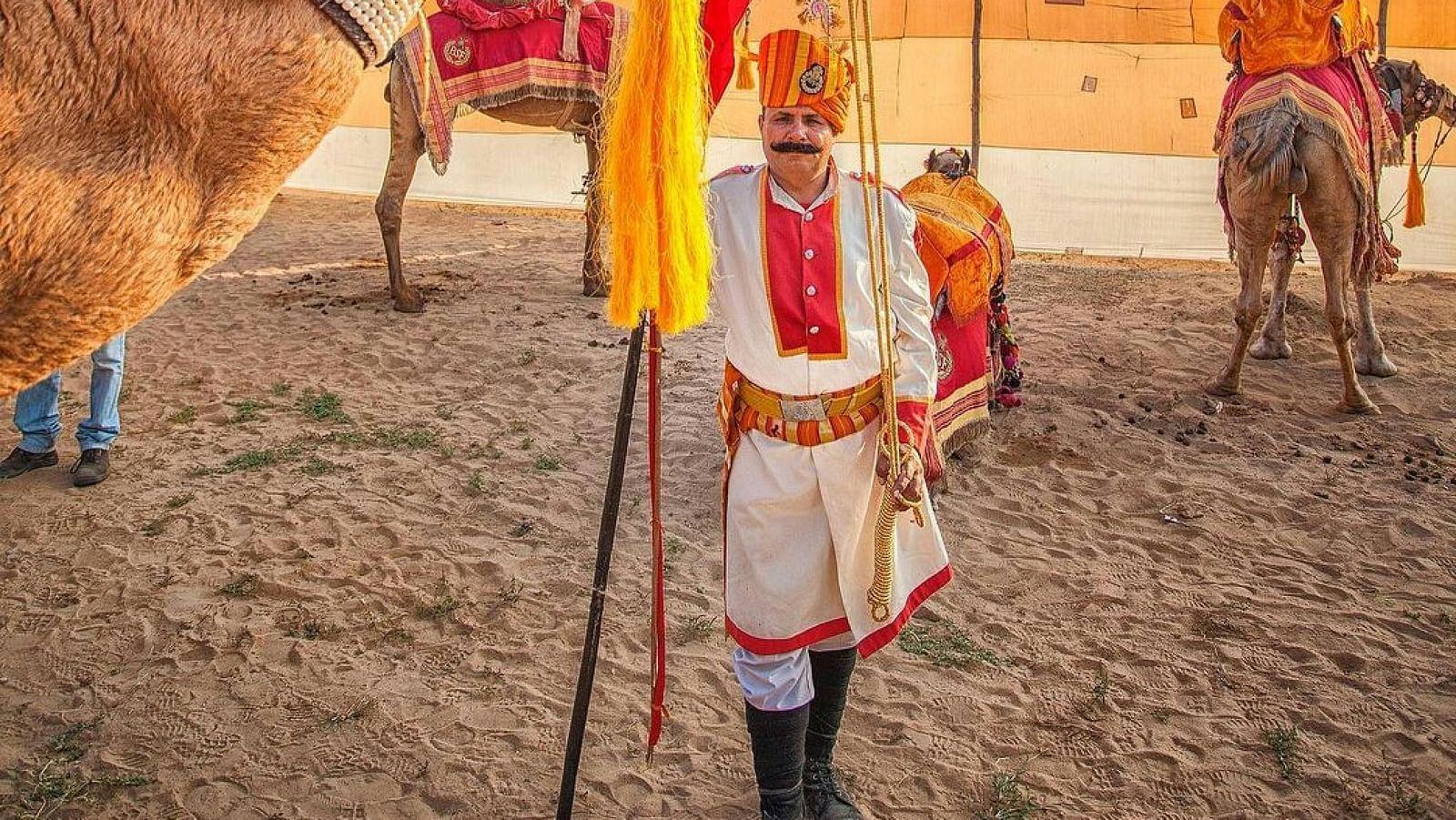 A camel rider in rajasthan holding on to a camel in the desert
