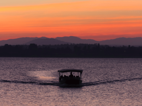 A boat cruising through a river during sunset with the hills visible in the background.