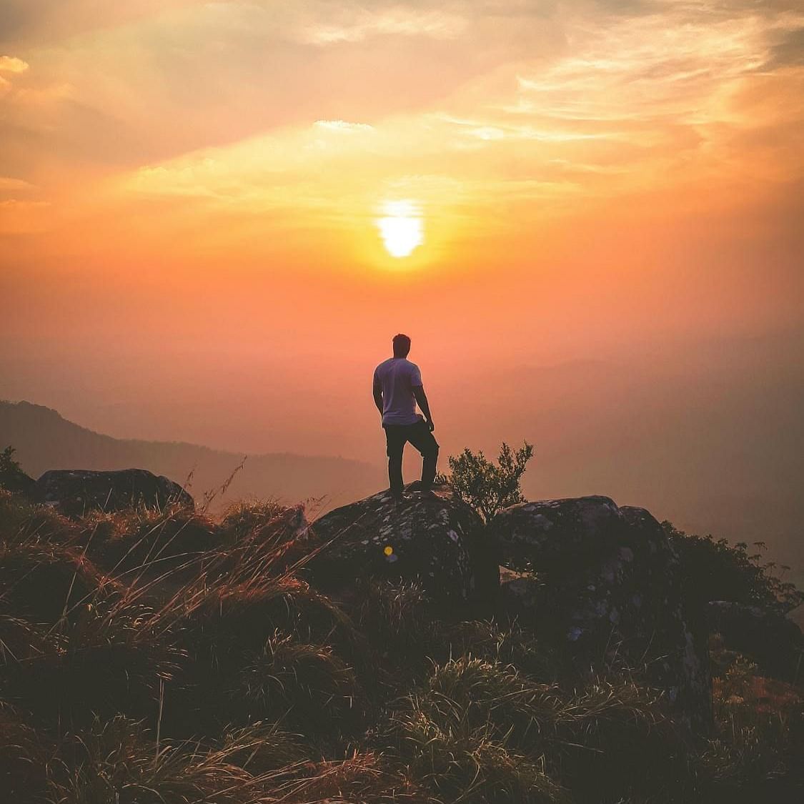 Image of a person standing on a cliff with the sun in front.