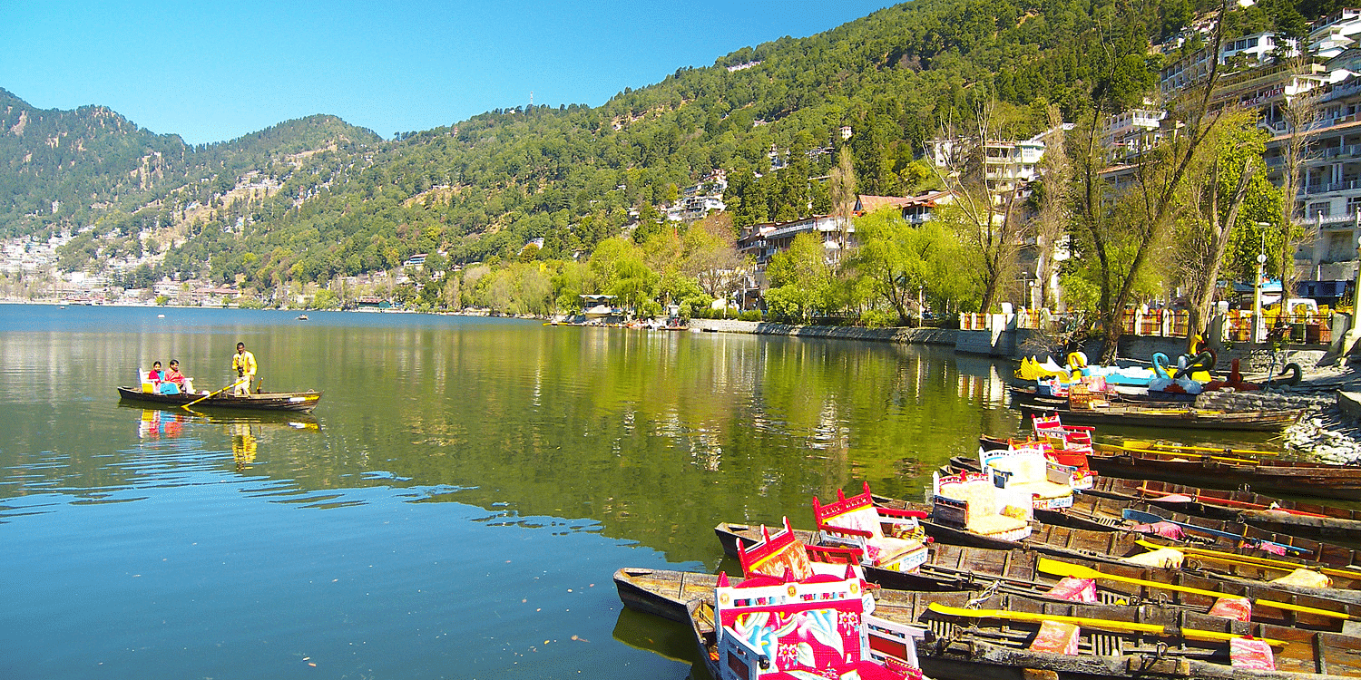 Wide view of a lake with boats standing on the shore and hills covered with trees in the distance
