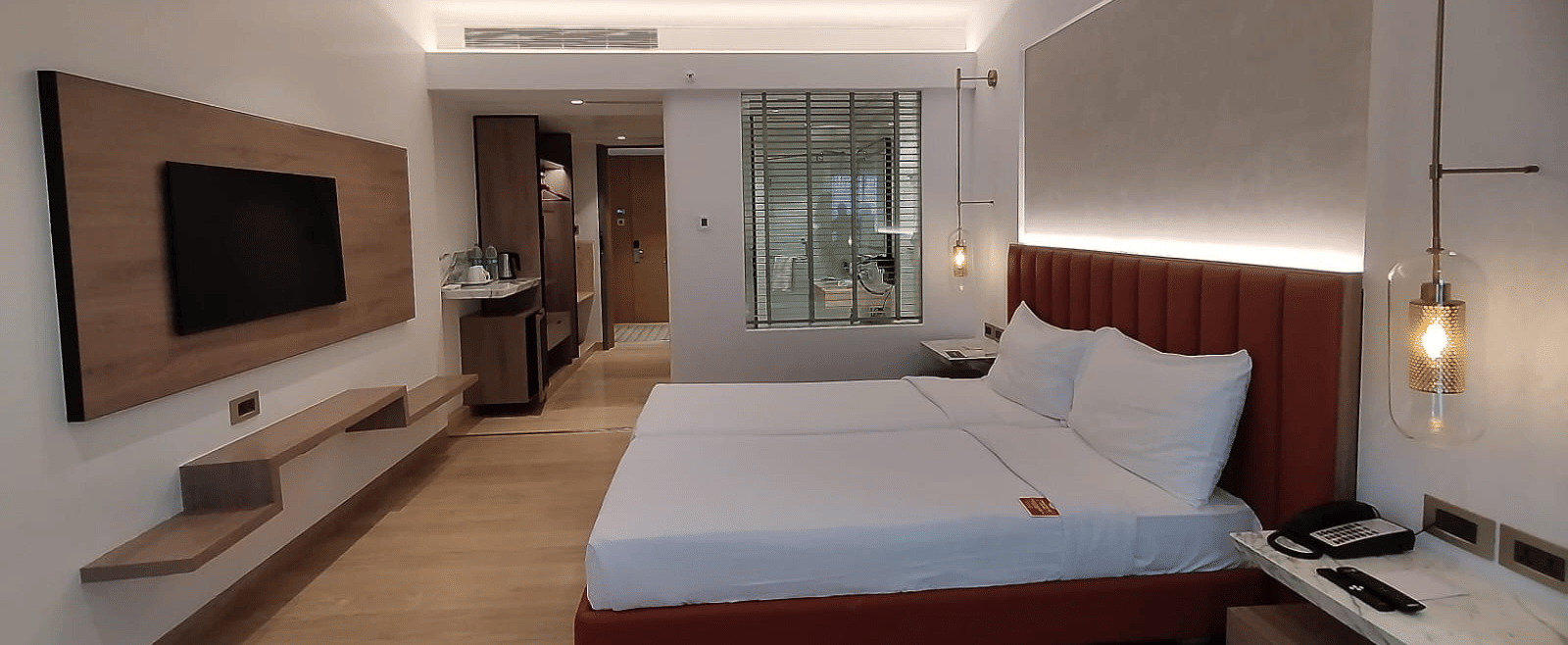 A well-lit, wooden floored, executive room in Mirage Hotel, featuring twin beds with decorative head-rest and a wooden panelled entertainment unit.