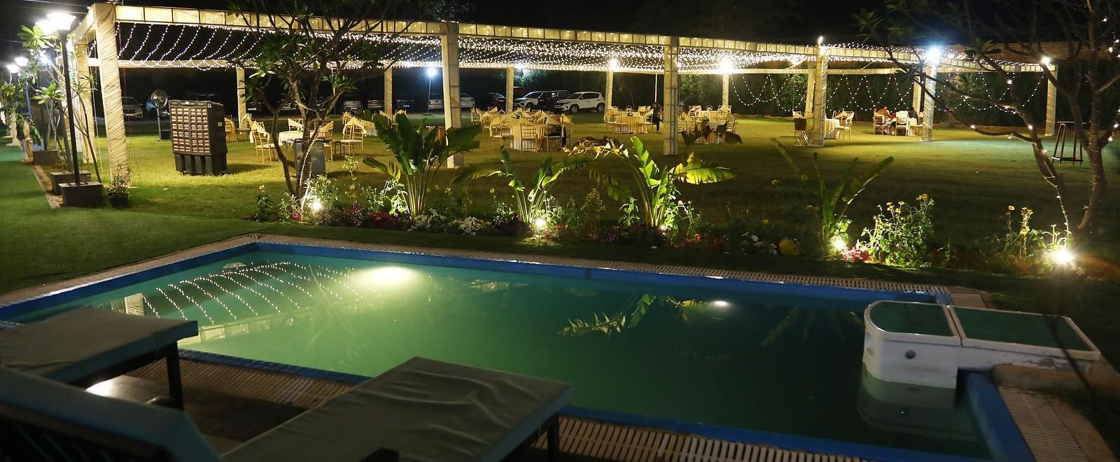 Swimming pool at Tisya Farms, Gurgaon with deck chairs and lighting, viewed during the night.