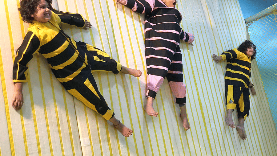3 excited kids hanging safely from the striped Velcro wall in their special jumpsuits at Tic Tac Tot.