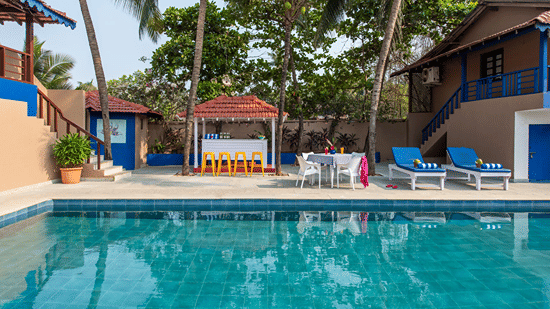 Outdoor swimming pool surrounded by palm trees, cottages and sun loungers.