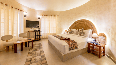 Boho Premium bedroom with backlit jute arch headboard and seating area at Valley by Grassfield, a resort in Jaipur.