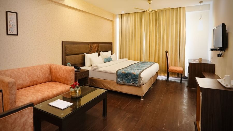 A bedroom with a neatly made bed, a peach-coloured sofa, and a small table, creating a comfortable space - VITS Gurugram