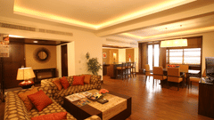 A hotel suite with sofas, tables, chairs, and warm lighting in the living area.