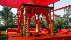 A ceremonial pavilion with decorative draping and pillars set up outdoors with palm trees in the background.