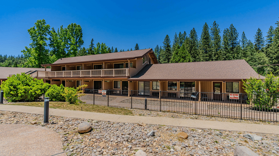 A view of a cabin at Amador Hotel with a forest in the backdrop on a clear, blue day.