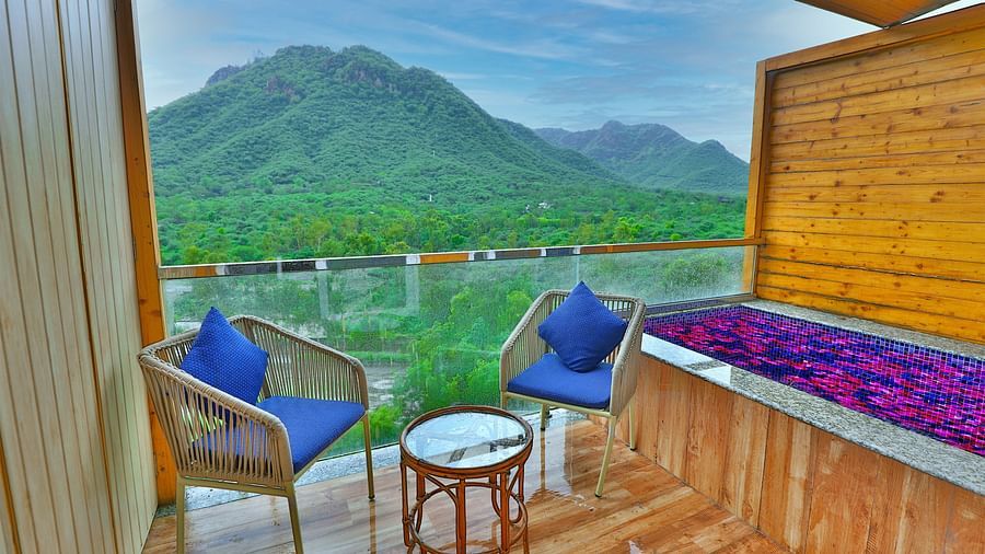 A balcony with two chairs, cushions, and a table with mountains as a scenery.- Bamboo Saa Resort & Spa, Udaipur