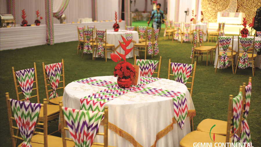 Round table close-up with a floral centrepiece, a floral print tablecloth, patterned chair covers and green lawn flooring beneath the table.