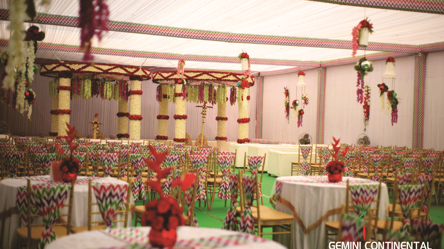 Outdoor lawn setup with round tables dressed in floral prints, patterned chair covers, hanging floral decor and a tented canopy overhead above.