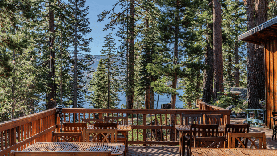 A wooden outdoor deck at Kit Carson Lodge featuring seating areas surrounded by towering pine trees and a view of the lake