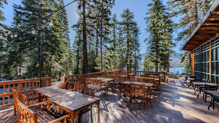 A spacious outdoor dining deck at Kit Carson Lodge with wooden tables and chairs surrounded by tall trees