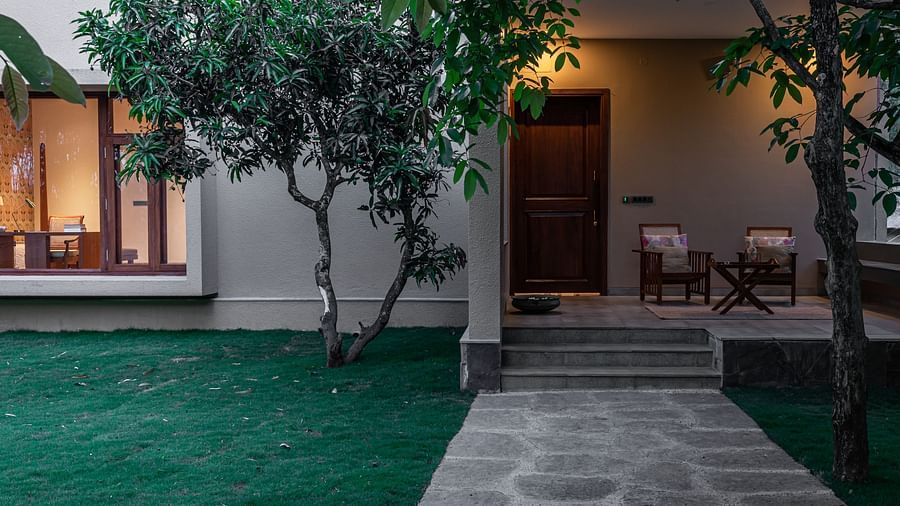 Exterior of a building with lit windows, trees, and a stone pathway at dusk - Shreyas Retreat