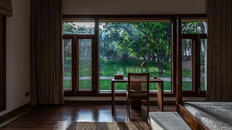 Living room with wooden table and chairs, large windows, garden view, bright interior - Shreyas Retreat