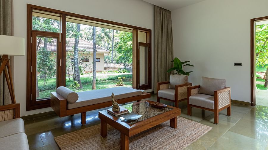 Living room with wooden furniture, rug, and large windows overlooking a garden, spacious interior - Shreyas Retreat
